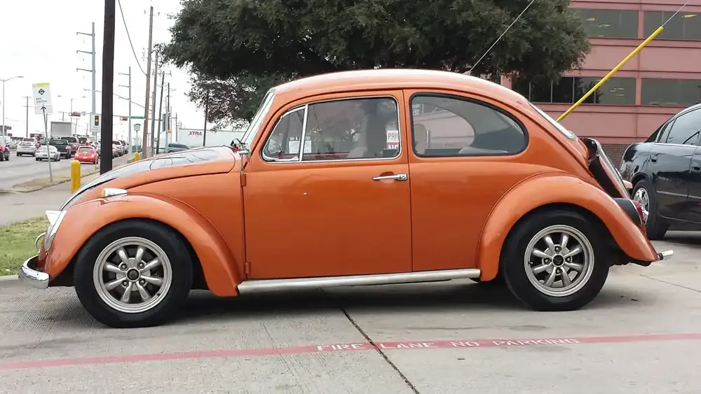 A restored orange classic Volkswagen Beetle parked near the shop